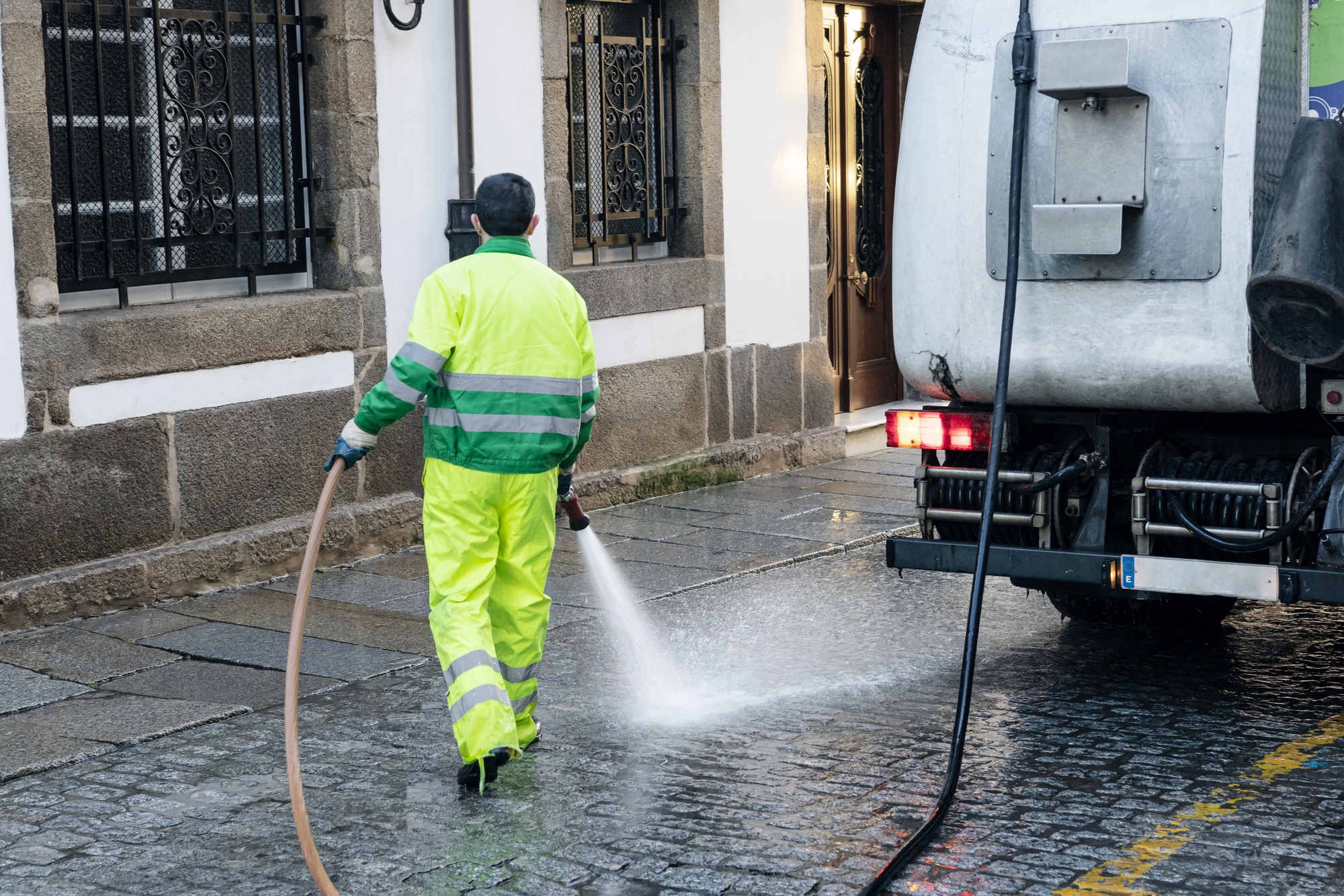 Worker cleaning with pressure water a street of a historic town